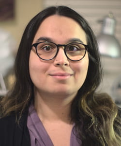 A portrait-style photo of a woman with glasses. A lamp is in the background.